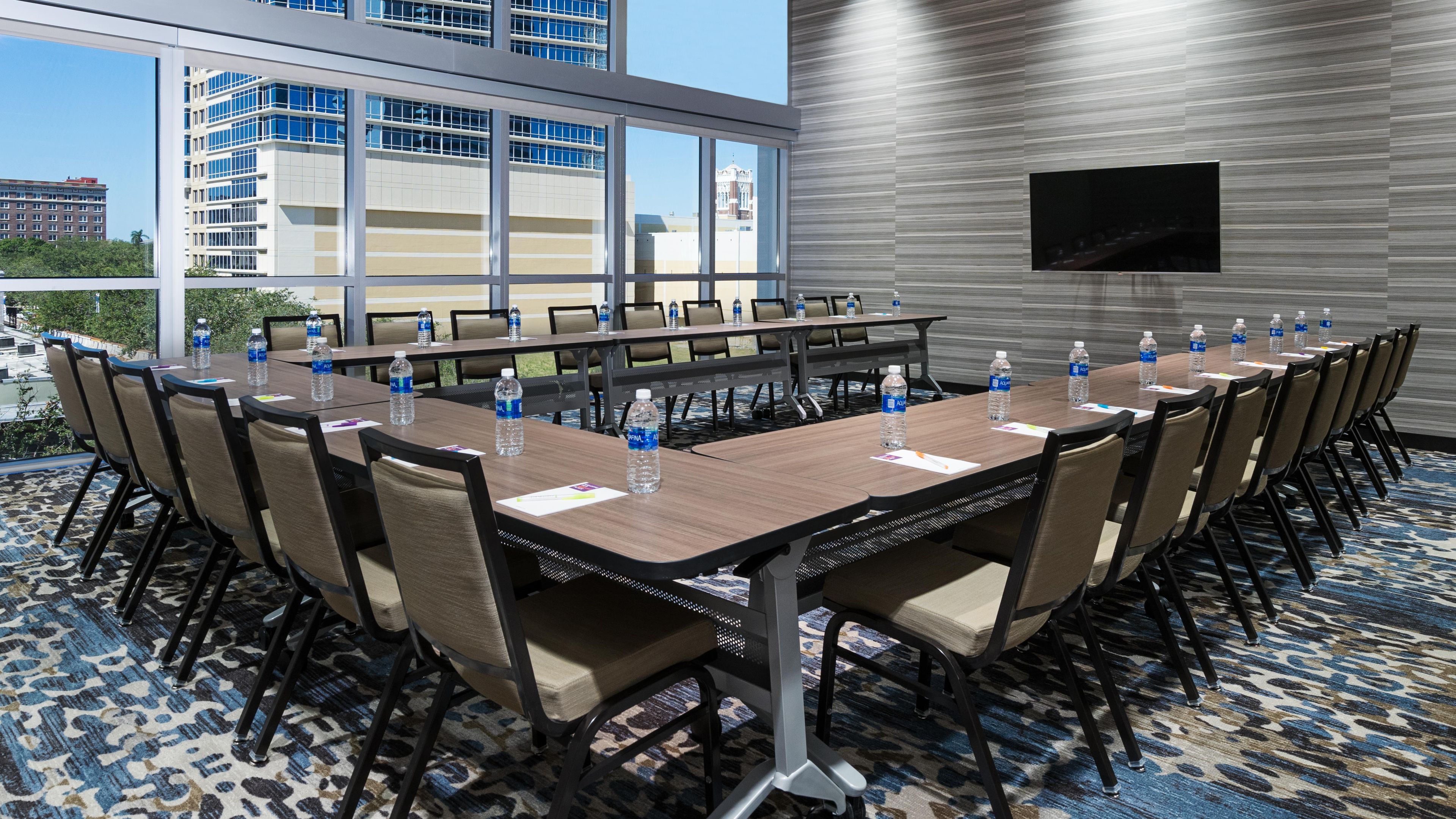 A conference room with a long table, chairs, water bottles, and a flat-screen TV on a wall.