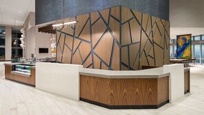 A modern reception desk with a geometric wood panel design, a marble countertop, and a large window with a cityscape view. - Hyatt Place St. Petersburg / Downtown (St. Petersburg)