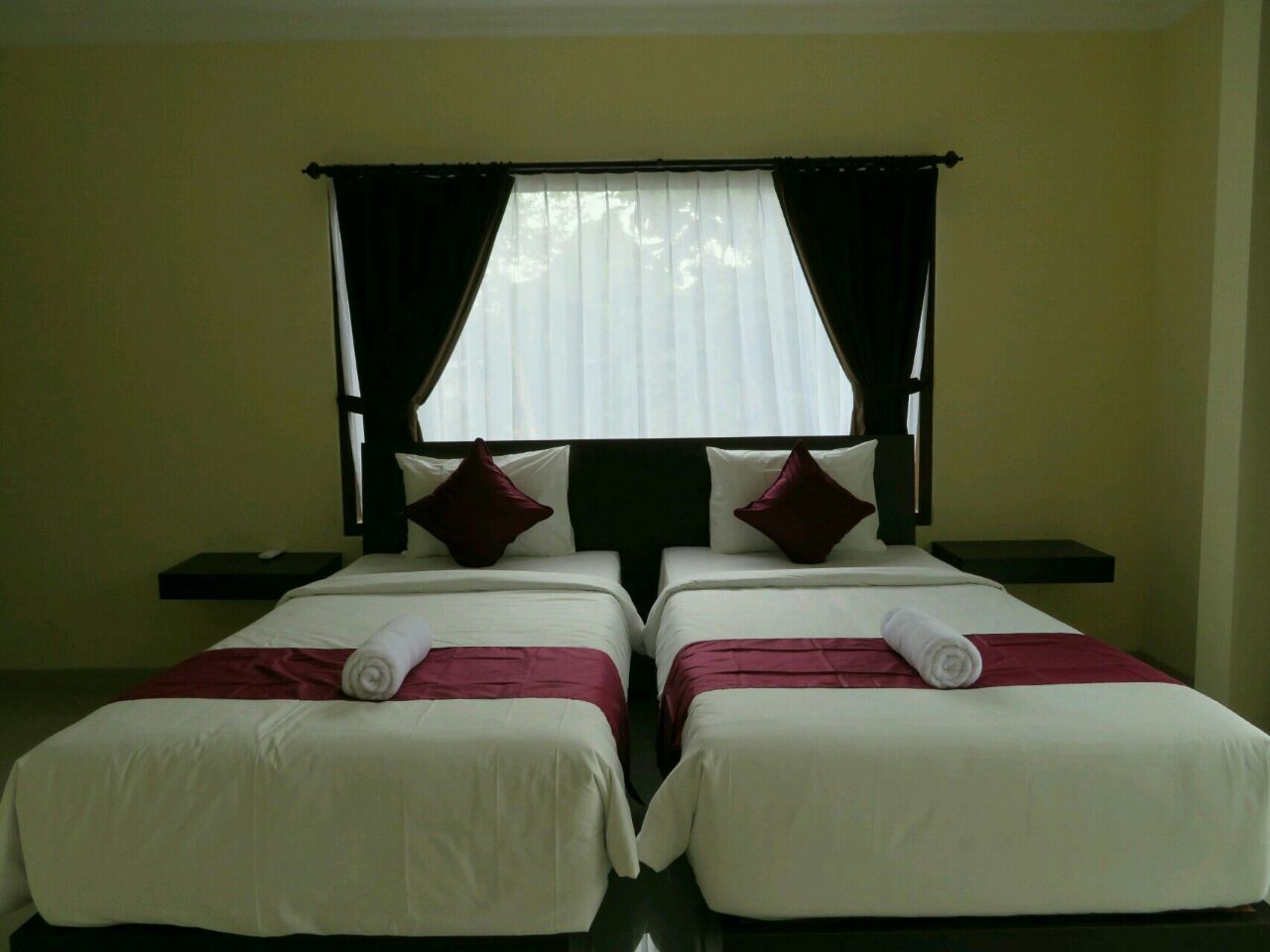 A hotel room with two single beds, a nightstand, a small table, and a window with curtains.
