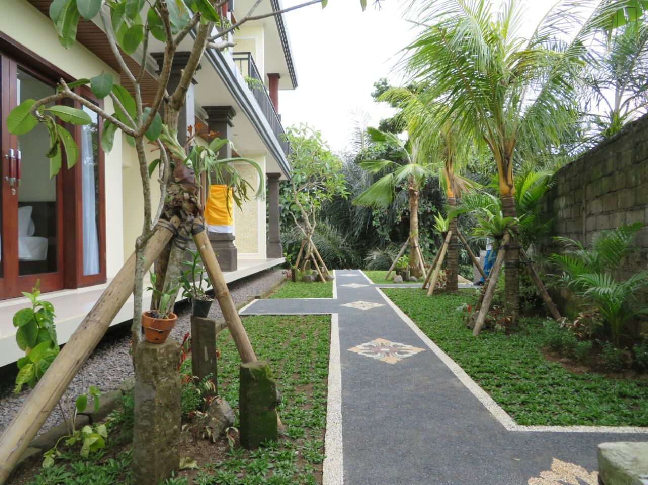 A pathway leading to a building with a balcony, surrounded by greenery and palm trees.