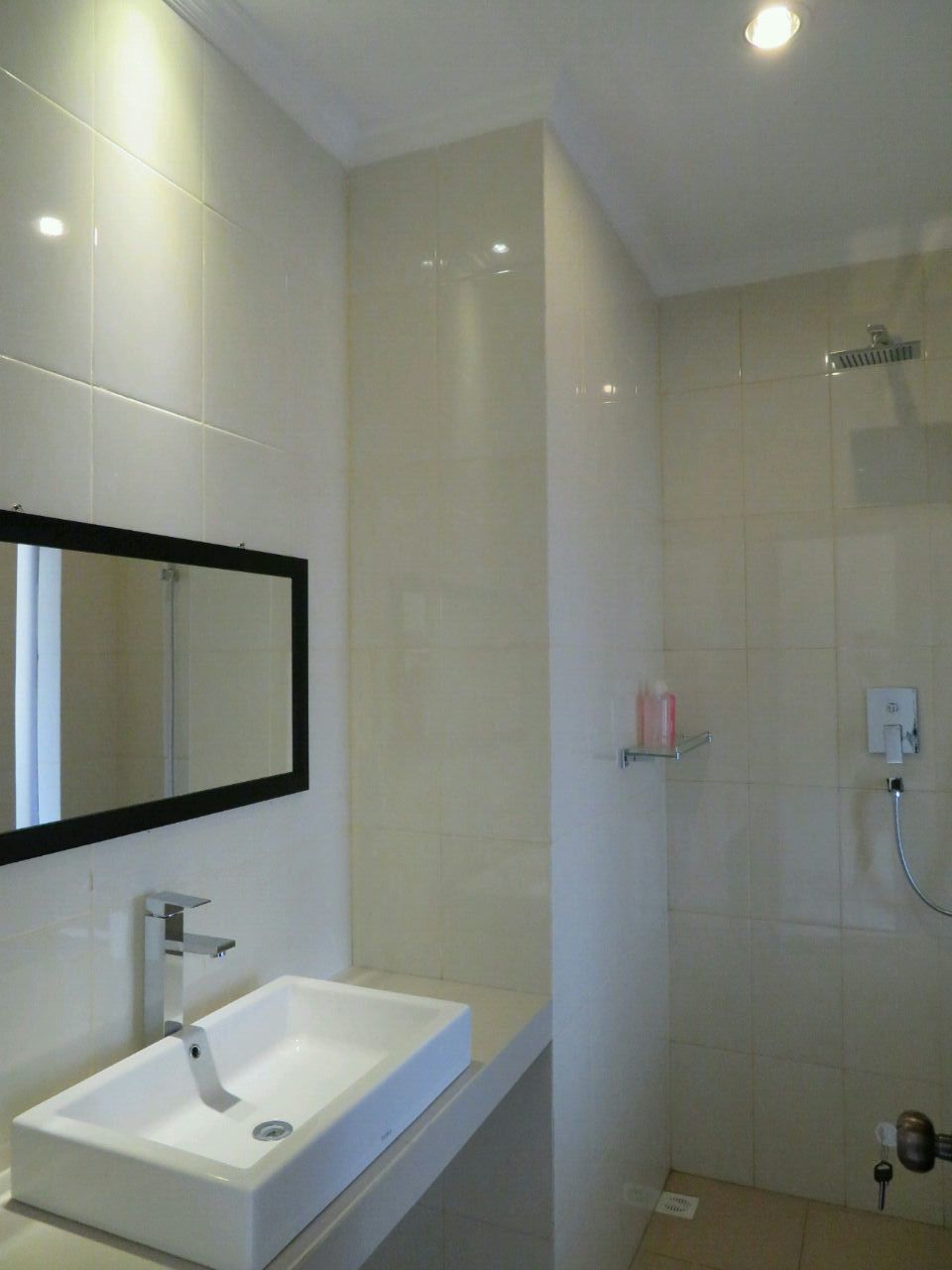 Un bagno moderno con un lavandino bianco, uno specchio grande e uno spazio doccia.