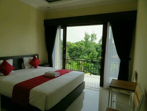 A hotel room with a large bed, a small table, and a balcony with a view of greenery. - Odah Ayu Guest House (Ubud)
