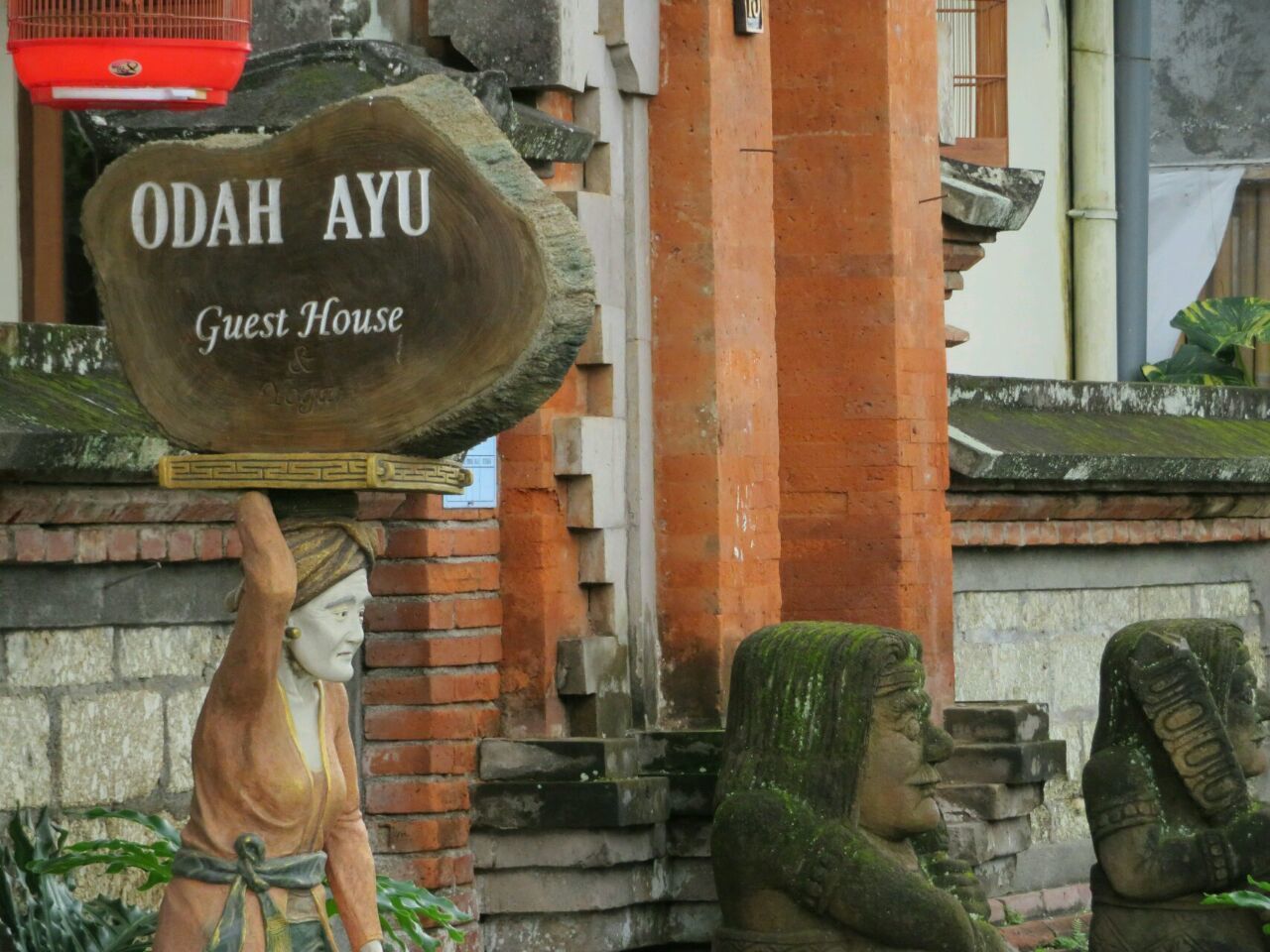 Señal para 'Odaah Ayu Guest House' con una estatua de una persona que porta una gran losa de piedra.