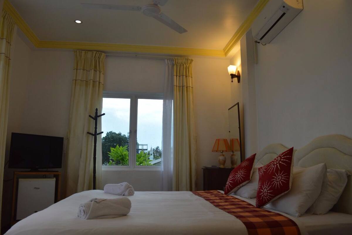 A hotel room with a bed, a television, a desk, and a window with curtains.