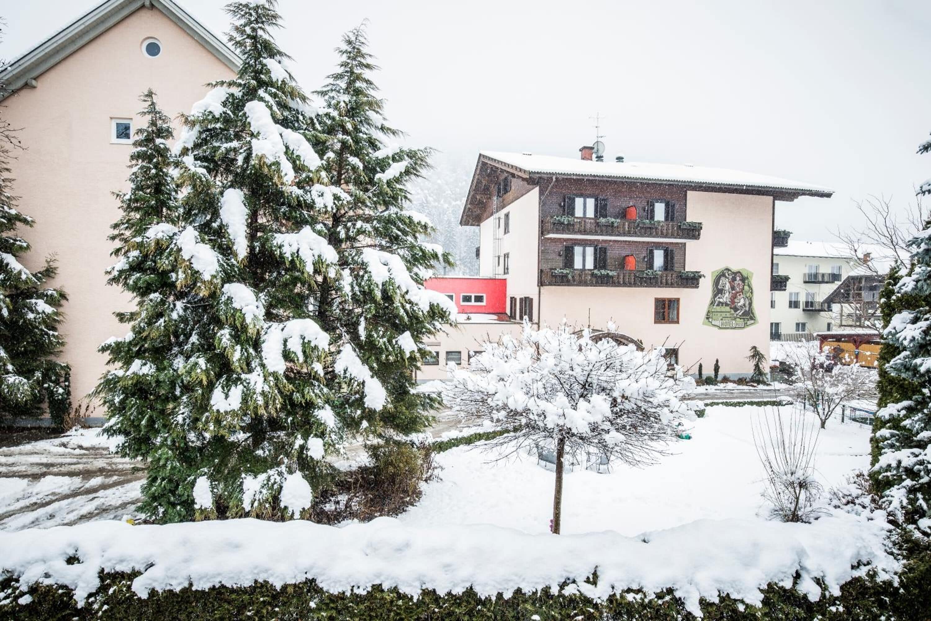 A building with a snow-covered garden and a red building in the background.