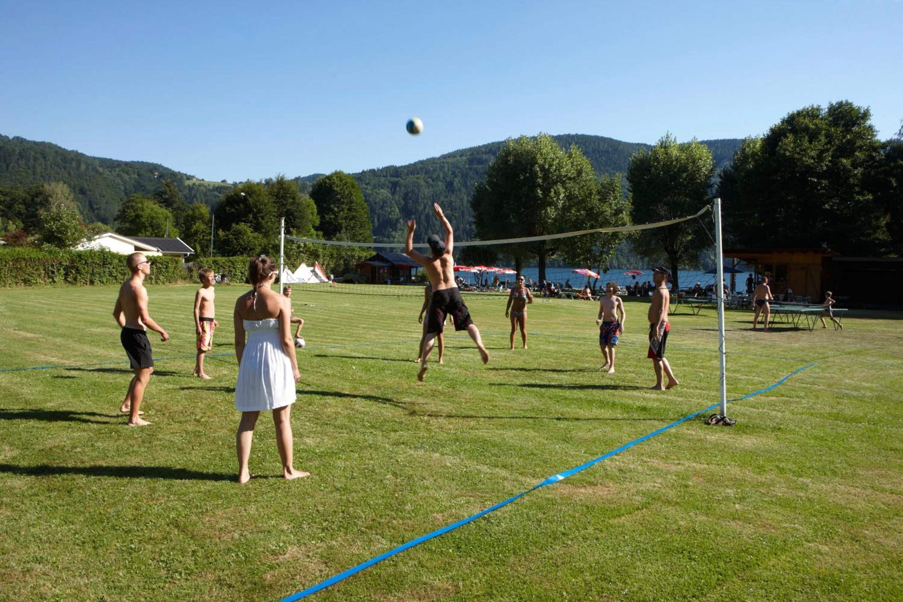 A group of people playing volleyball on a grassy field with a net.