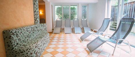 A sunlit lounge area with a checkered floor, a patterned sofa, and several lounge chairs.