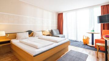 Habitación de hotel con una cama grande, un escritorio, una silla, un televisor y una ventana con cortinas.