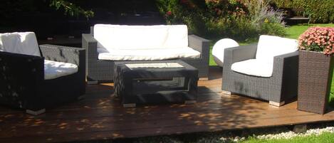 An outdoor patio with wicker furniture, including a sofa, two armchairs, and a small table.