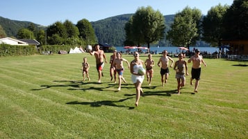 A grassy field with people running, a lake, and trees in the background.
