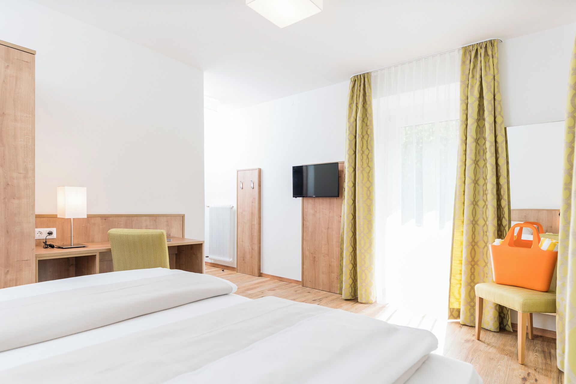 Ein Hotelzimmer mit zwei Betten, einem Schreibtisch mit Stuhl, einem Fernseher und einem Fenster mit Vorhängen.