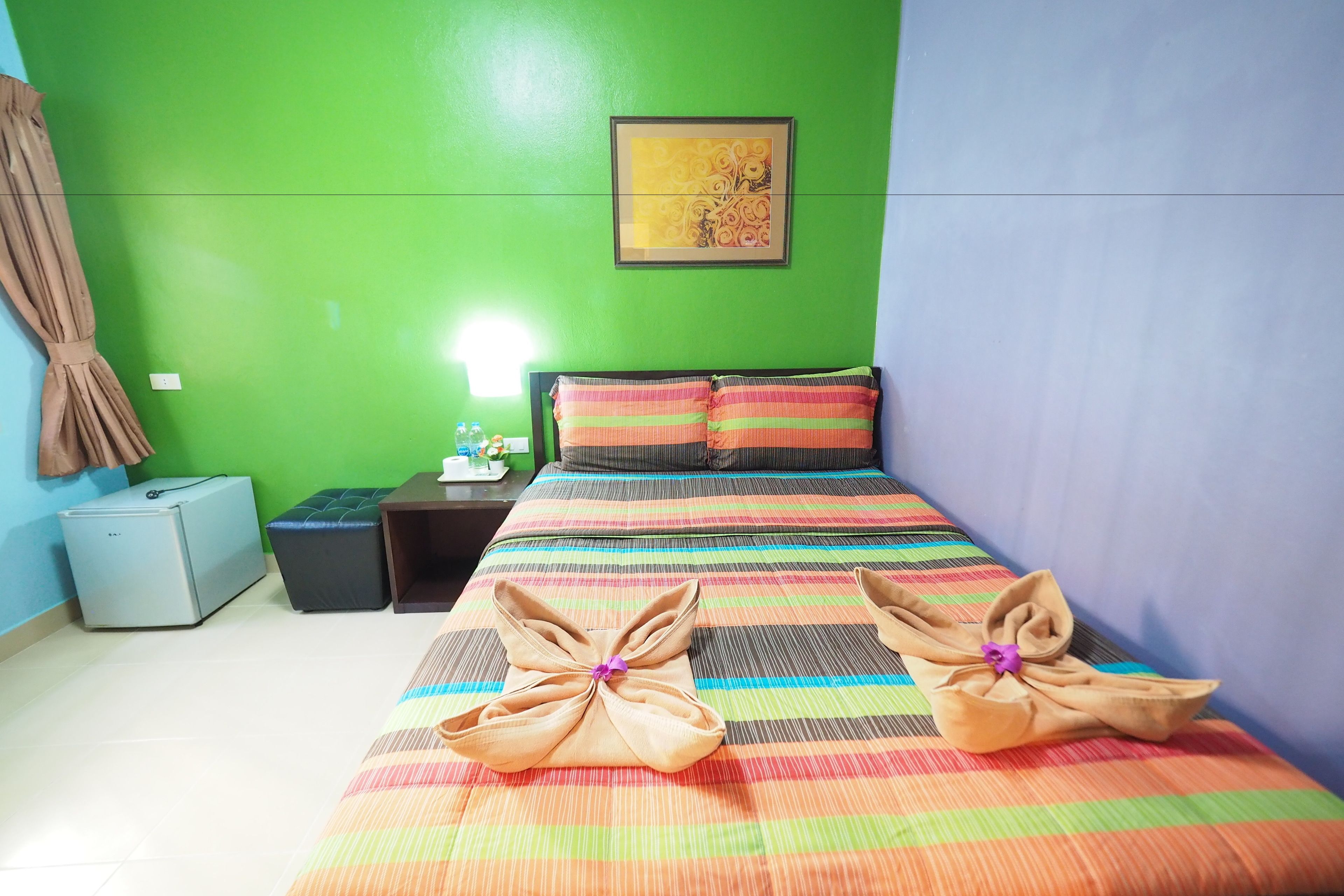 A room with a bed, green walls, a framed picture, a nightstand, a lamp, and a small refrigerator.