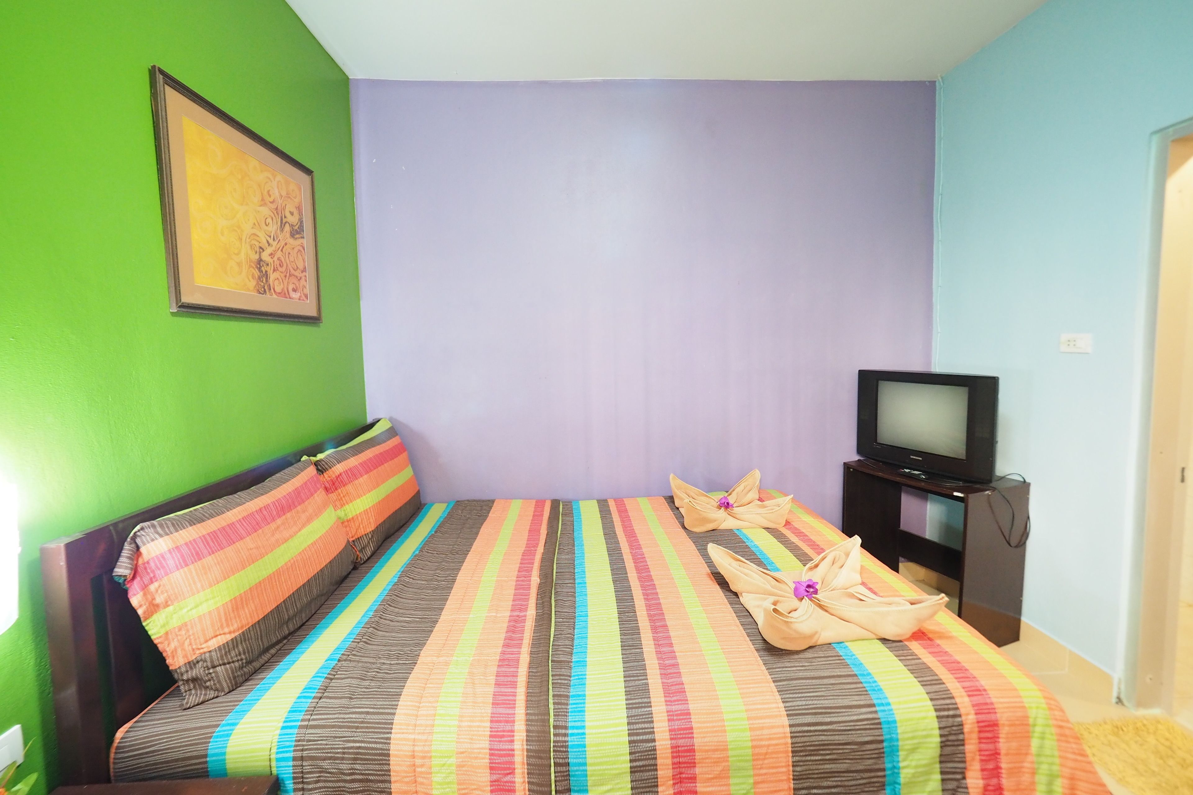 Une chambre avec un lit, une télévision et un tableau au mur.