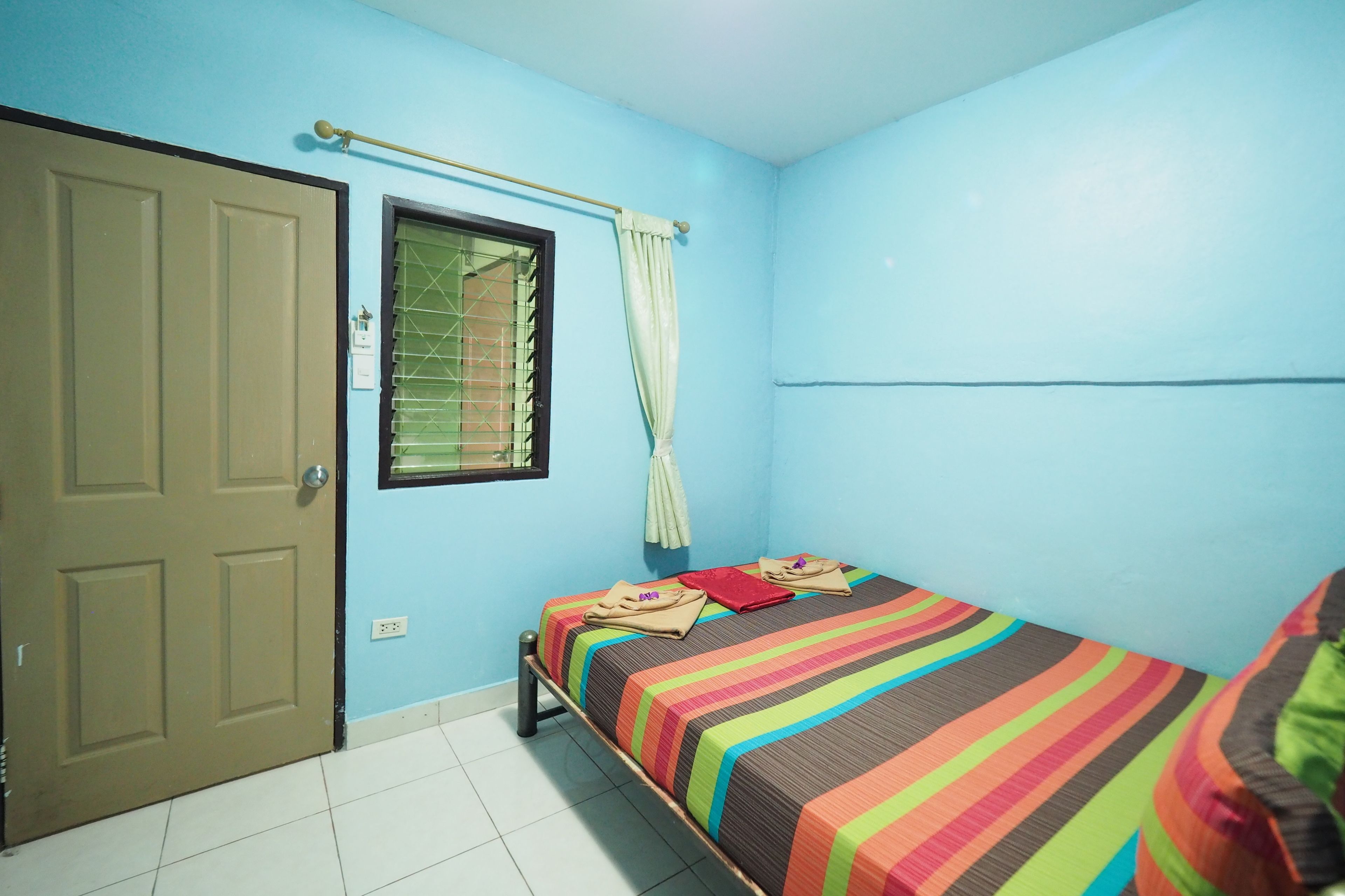 A room with a single bed, a window with curtains, a door, and a tiled floor.