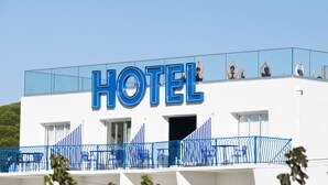 A hotel with a prominent "HOTEL" sign, a balcony with blue chairs, and a clear sky. - La Reine Jane (Hyères)