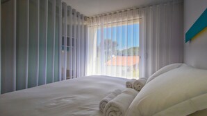 A hotel room with a large bed, white linens, and a view of a building through sheer curtains. - La Reine Jane (Hyères)