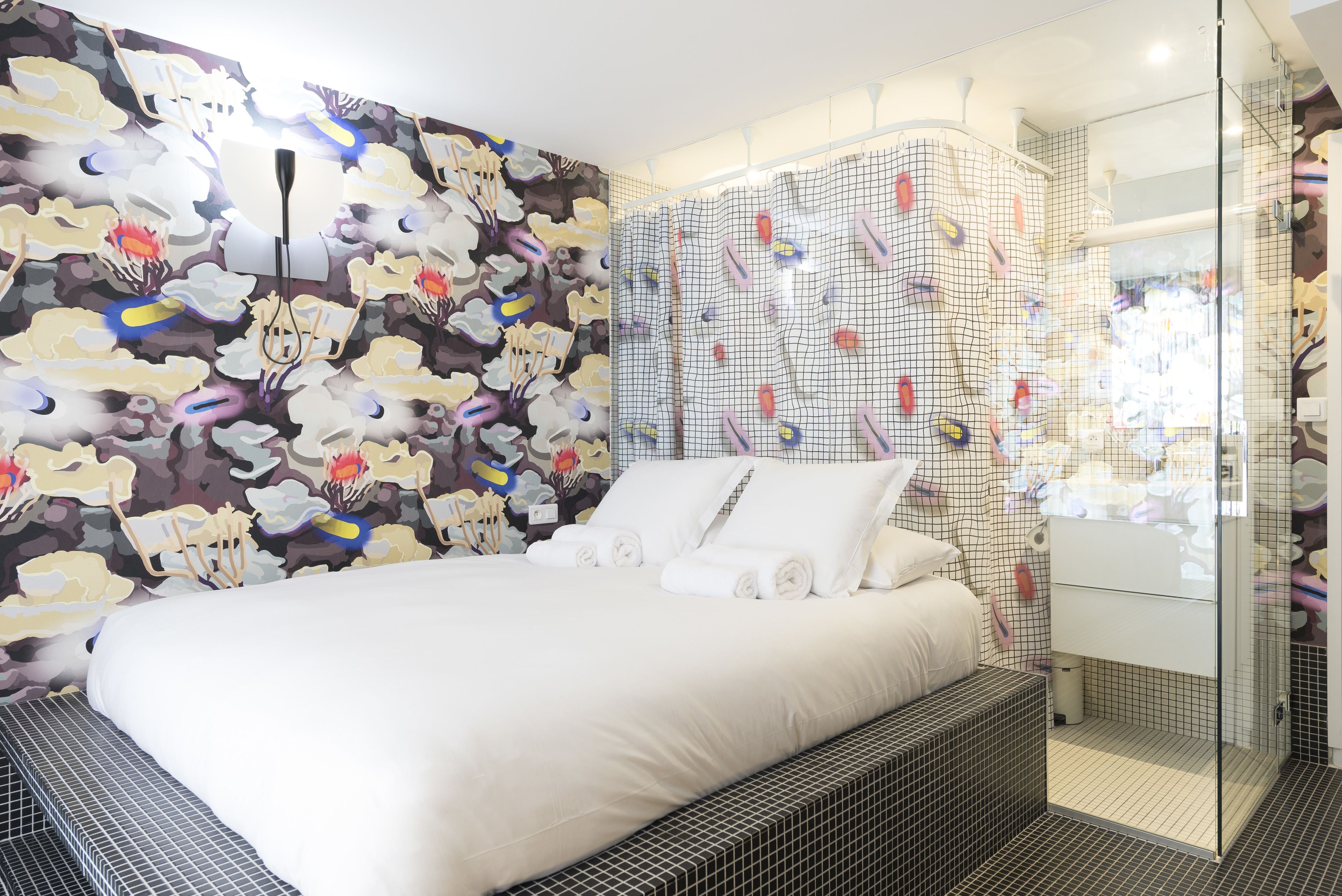 A modern hotel room with a large bed, a shower area with a glass enclosure, and a wall with a floral mural.