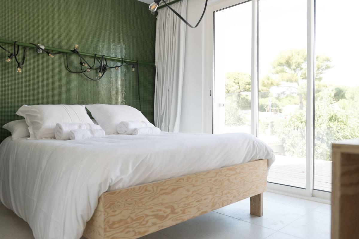 Un dormitorio moderno con una cama grande, una pared verde y vistas al exterior.