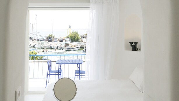 A modern bathroom with a bathtub, a round mirror, and a view of a marina through an arched doorway. - La Reine Jane (Hyères)
