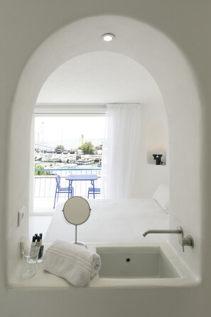 A modern bathroom with a bathtub, a round mirror, and a view of a marina through an arched doorway. - La Reine Jane (Hyères)