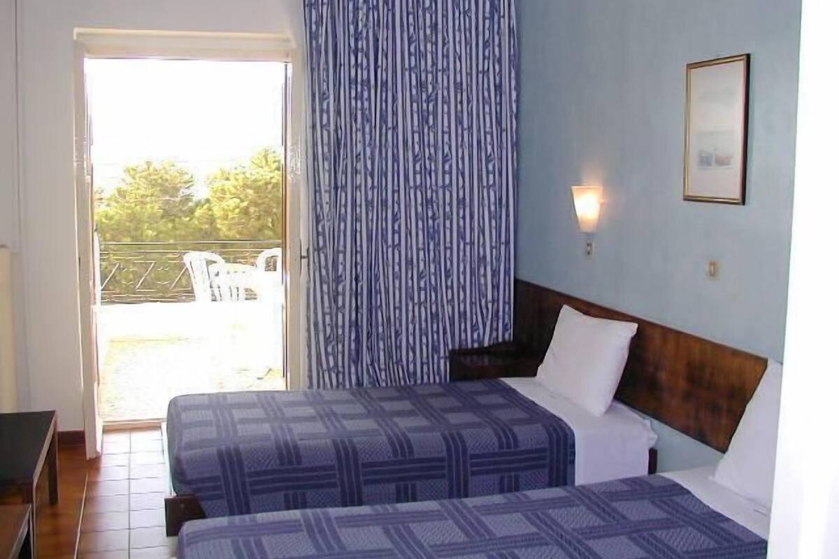 Habitación de hotel con dos camas, cabecero de madera, ventana con cortinas y una lámpara fijada a la pared.