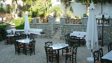 An outdoor patio with stone walls, multiple tables and chairs, and umbrellas.