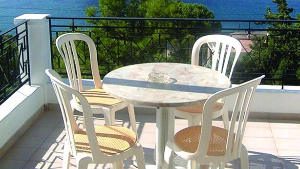 A terrace with a table and chairs overlooking a body of water and a mountain. - Oasis Hotel (Kalymnos)