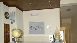 A reception desk with a wooden finish, a globe, and a sign above it that reads "Reception". - Oasis Hotel (Kalymnos)