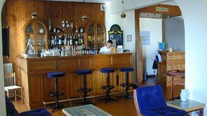 A bar area with wooden paneling, a bartender, and stools. - Oasis Hotel (Kalymnos)