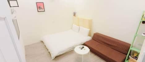 A small, clean room with a bed, a brown sofa, a small round table, and a green shelf.
