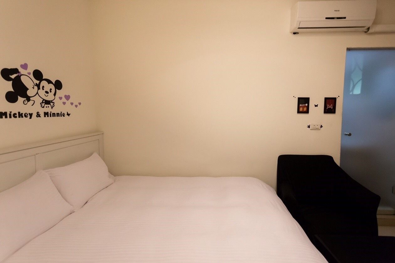 A hotel room with a bed, a Mickey & Minnie wall decal, a black chair, and a door.