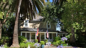 A house with a porch, surrounded by various plants and trees. - The Giraffe Inn at Old Parks Manor (Napa)