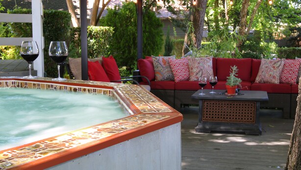 A hot tub with a tiled edge, a red sofa with patterned cushions, and two wine glasses on a table. - The Giraffe Inn at Old Parks Manor (Napa)