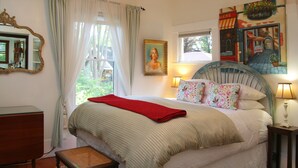 A bedroom with a bed, a bedside table, a lamp, a chair, a window, and a painting on the wall. - The Giraffe Inn at Old Parks Manor (Napa)