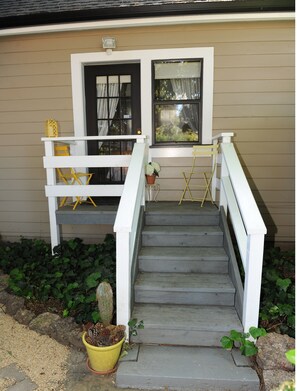 A house with a front porch, a staircase, and a small garden area with plants and a cactus.