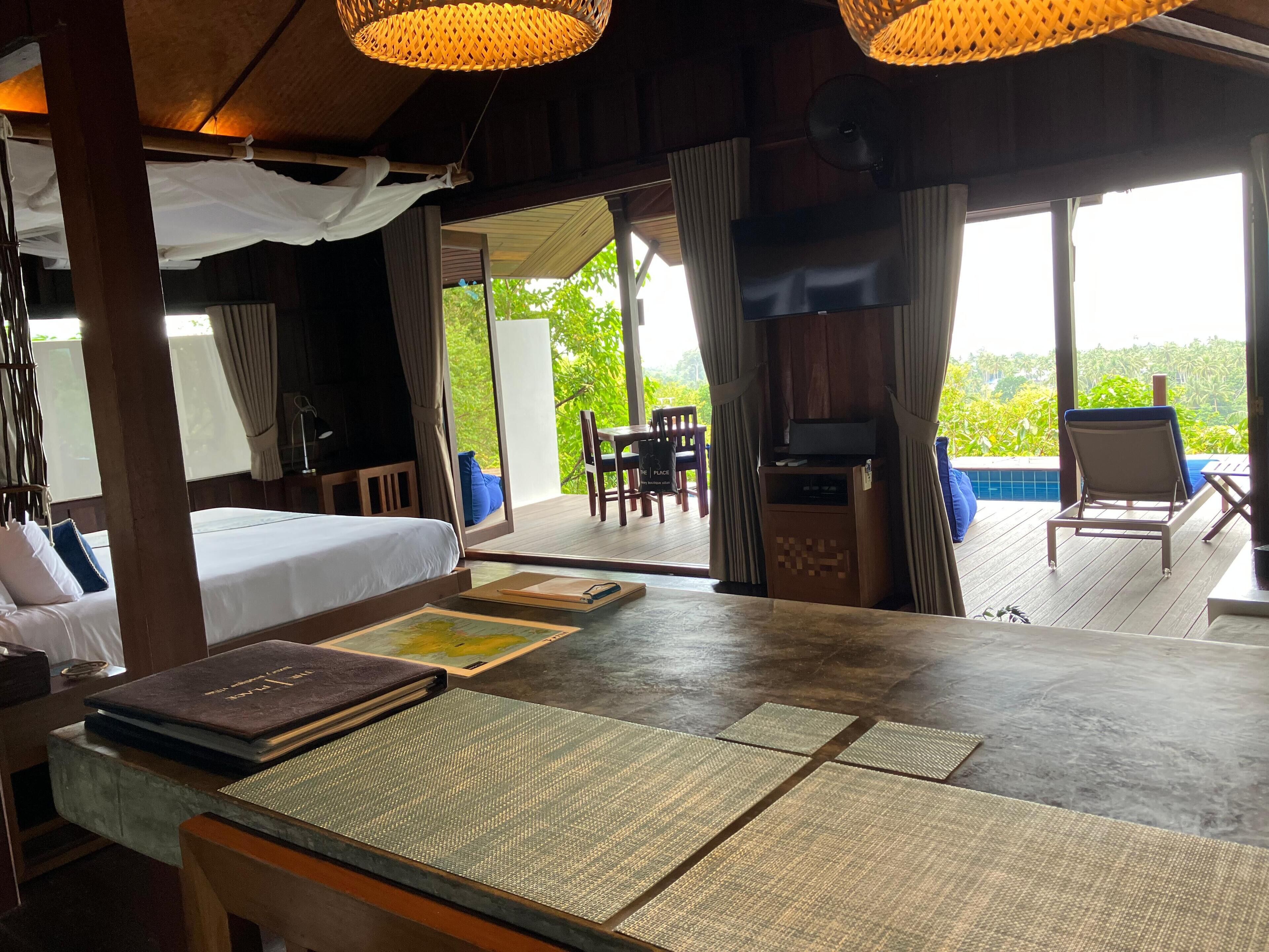 A room with a bed, a table with a book, a TV, and a view of greenery outside.