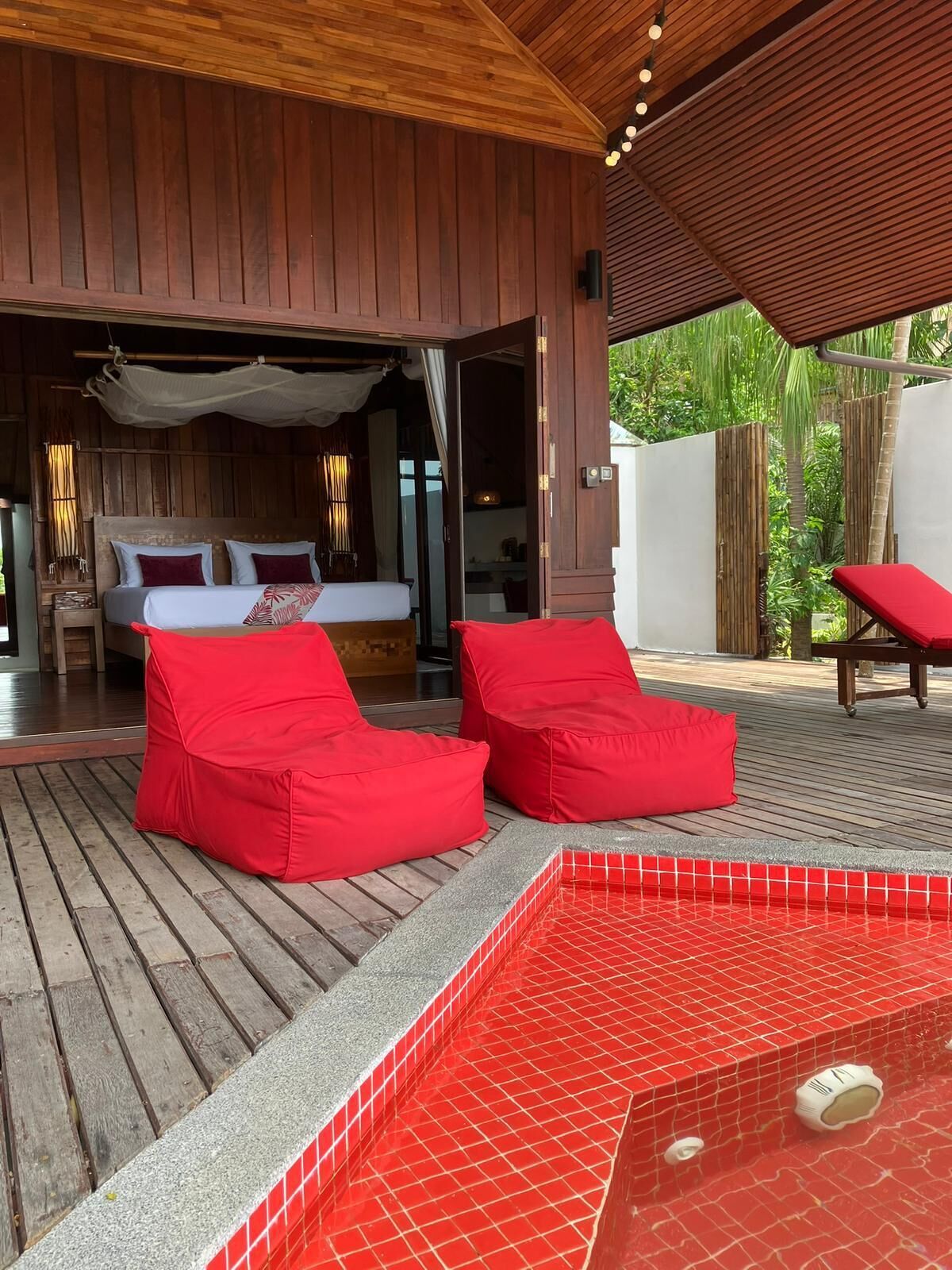 A wooden deck with a red-tiled hot tub, red bean bags, and a bed with white bedding.