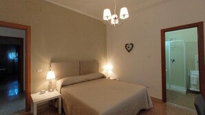 Un dormitorio con cama, lámparas de noche, una araña y una decoración con forma de corazón, además de una puerta que da al baño.