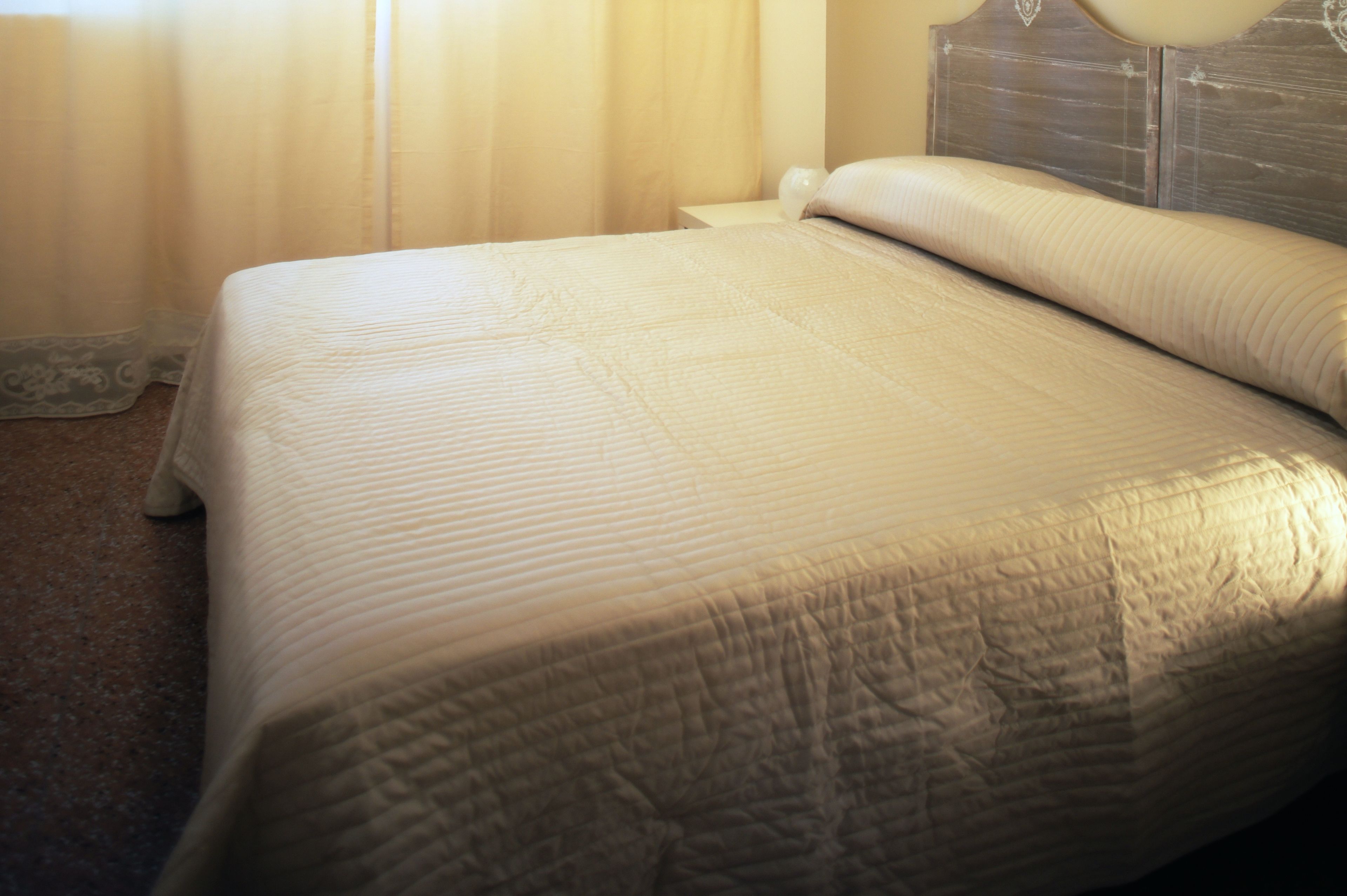 A neatly made bed with a quilted cover and a wooden headboard.