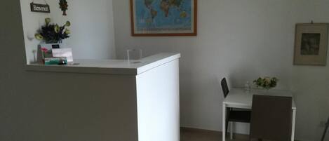 A small, clean room with a white reception desk, a dining table with two chairs, a world map on the wall, and a framed picture.