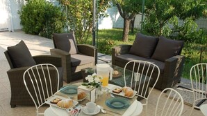 Un área de comedor al aire libre con mobiliario de mimbre, una mesa de vidrio y una jarra de jugo de naranja.