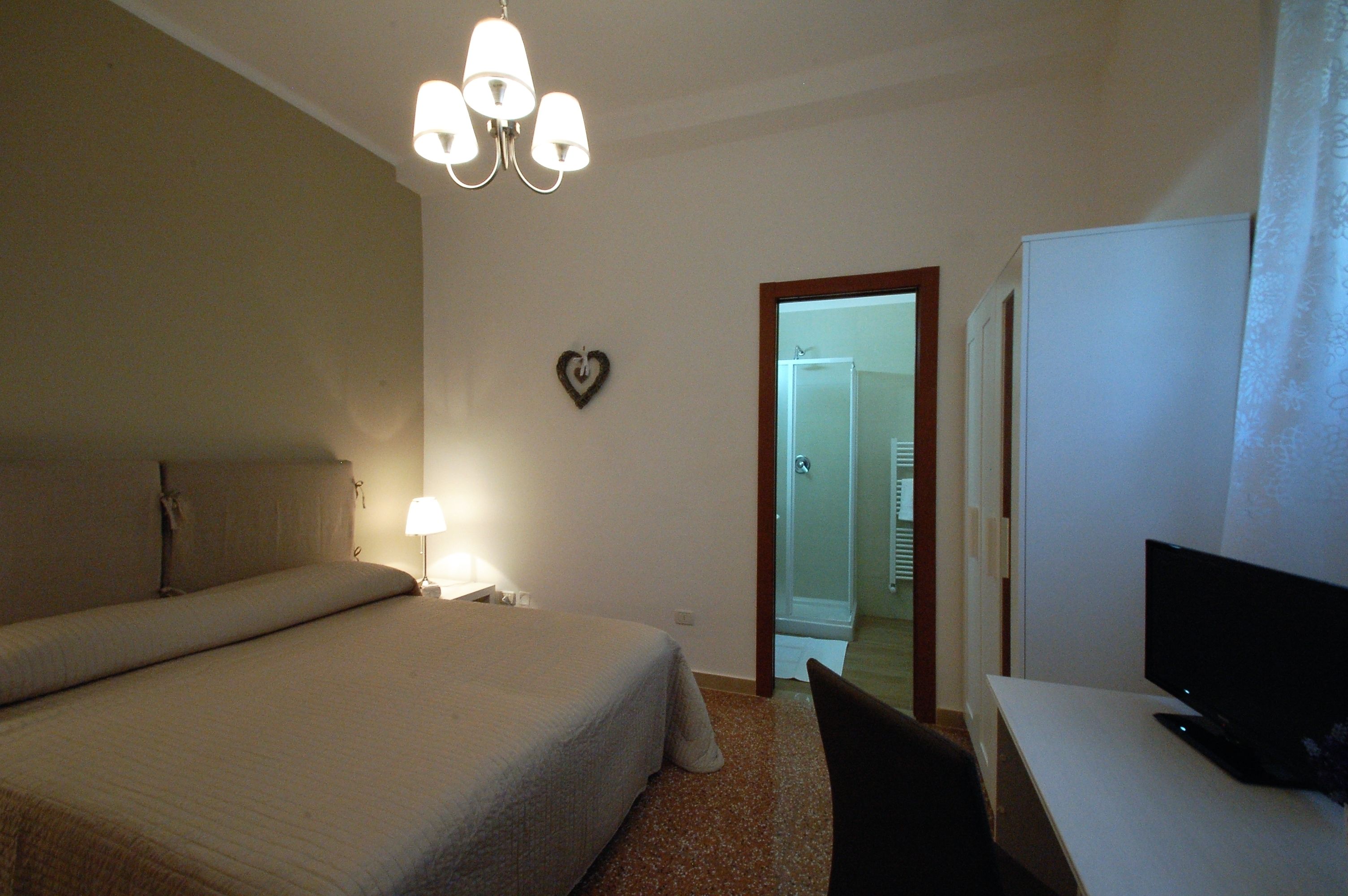 Una habitación de hotel con una cama, un escritorio con televisor, una lámpara y una decoración con forma de corazón en la pared.