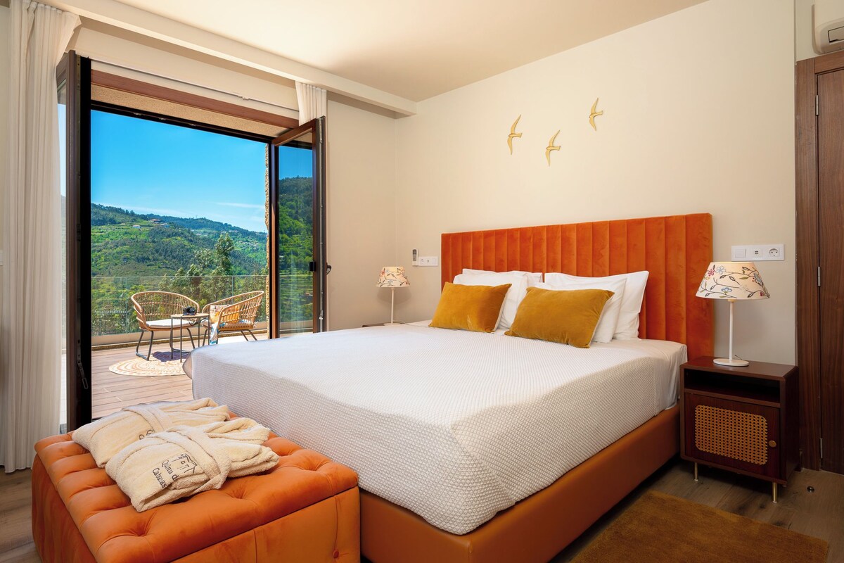 Een hotelkamer met een groot bed, een slaapbank, een balkon met stoelen en uitzicht op het platteland.