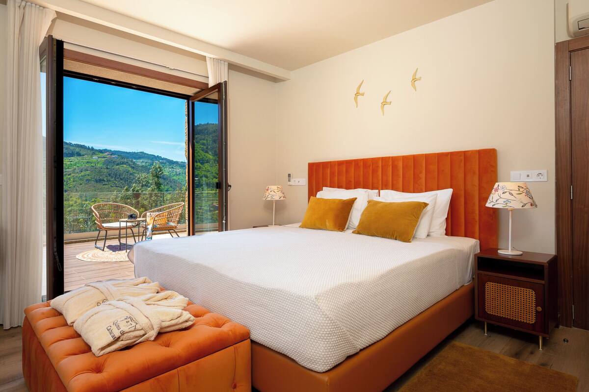 Een hotelkamer met een groot bed, een slaapbank, een balkon met stoelen en uitzicht op het platteland.