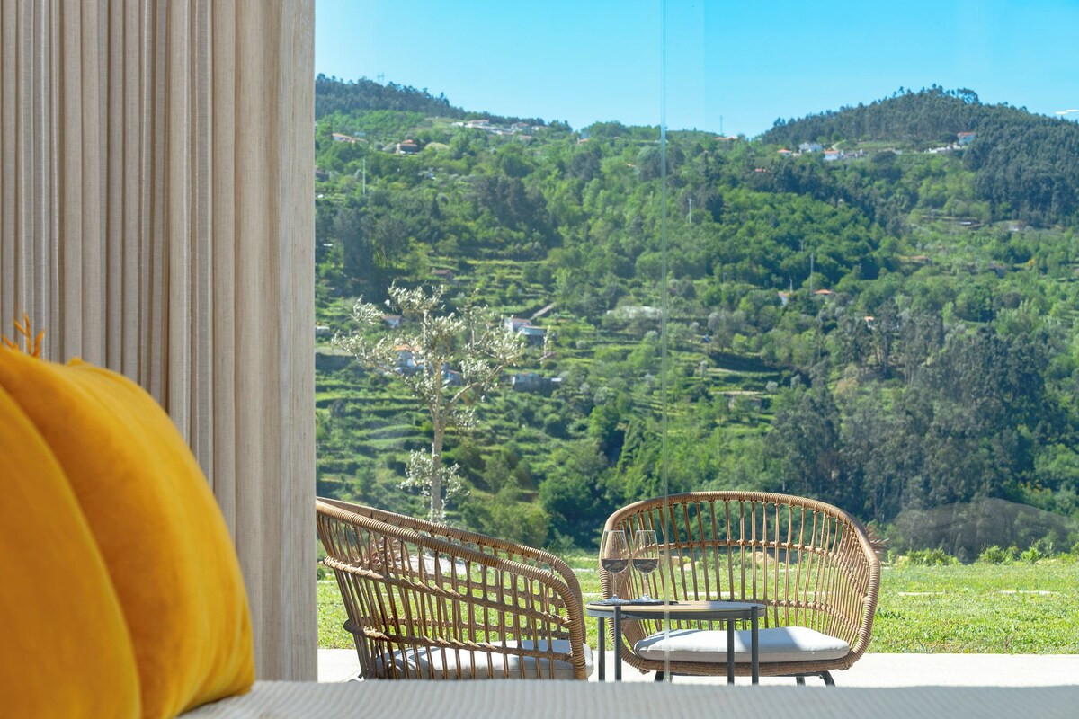 Een rieten stoel en tafeltje op een balkon met uitzicht op terrassen en heuvels.