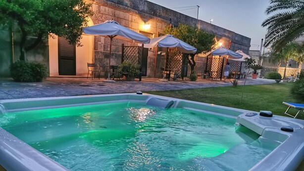 A swimming pool with a greenish tint, surrounded by outdoor seating areas with umbrellas, a stone wall, and a well-maintained lawn. - Villa Papaleo (Bagnolo del Salento)