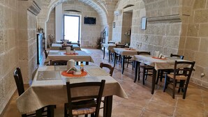 A restaurant with stone walls and arched ceilings, featuring multiple tables with chairs and a television screen on the wall. - Villa Papaleo (Bagnolo del Salento)