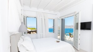 Ein Schlafzimmer mit einem großen Bett, weißen Vorhängen und Meerblick durch offene Türen.
