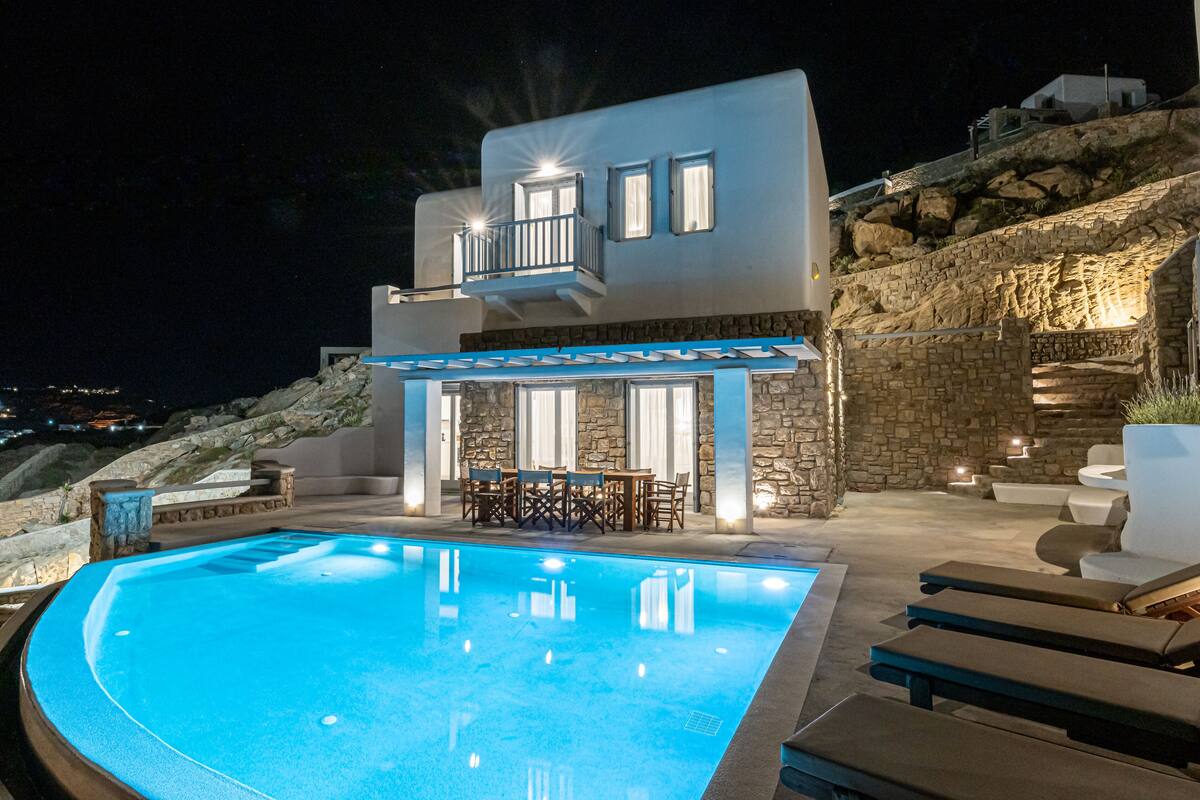 A modern villa with a swimming pool, outdoor seating, and stone walls.