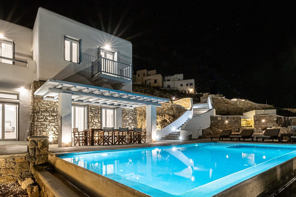 A modern building with a pool, stone walls, and a staircase leading to a balcony.